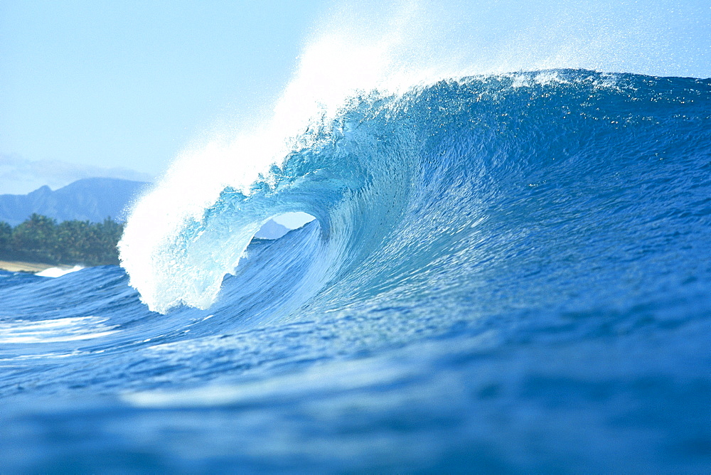 Side view of large wave with curl breaks toward shoreline spray off tips 