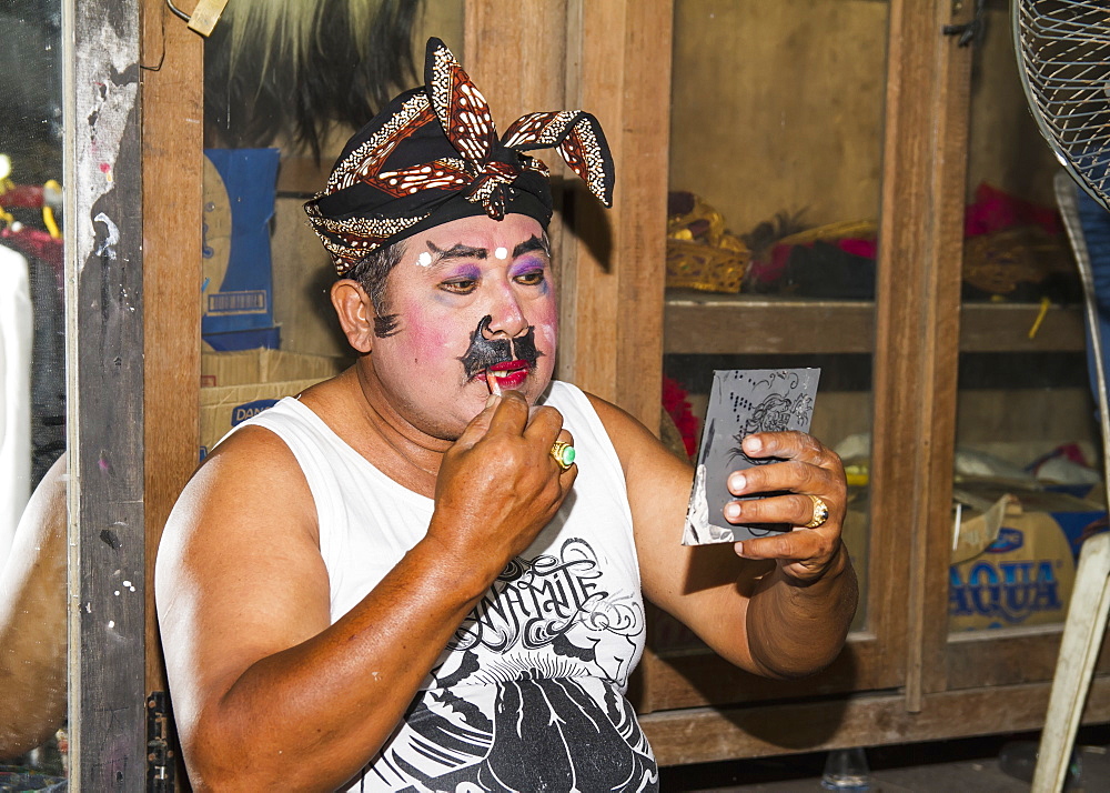 Balinese performer of the Raja Peni troupe applying make-up before a dance performance in front of a mirror, Ubud, Bali, Indonesia