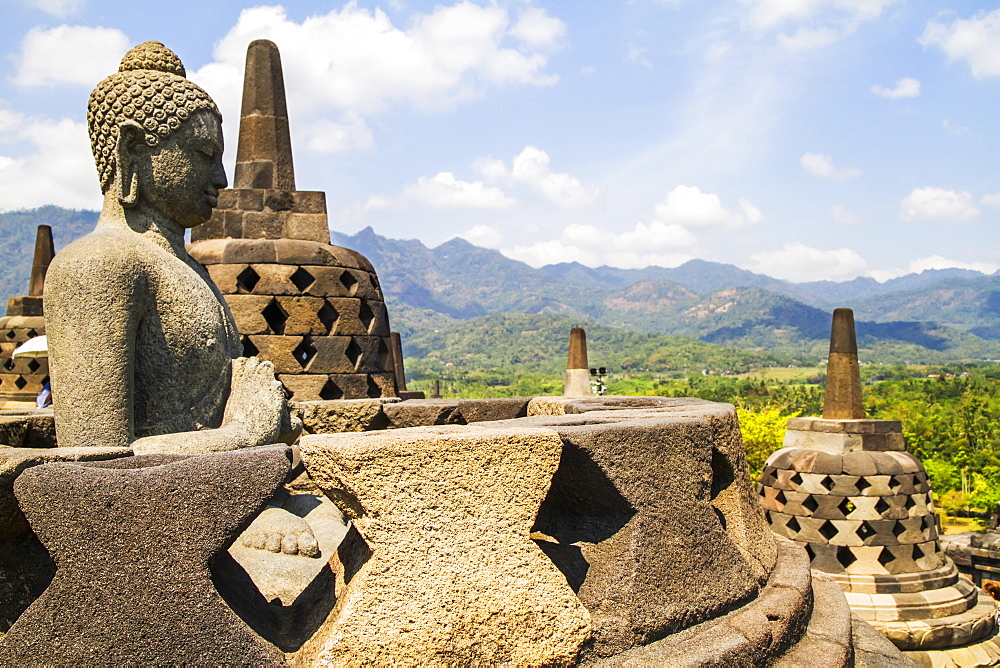 Buddha statue amidst the latticed stone stupas containing Buddha statues on the upper terrace, Borobudur Temple Compounds, Central Java, Indonesia