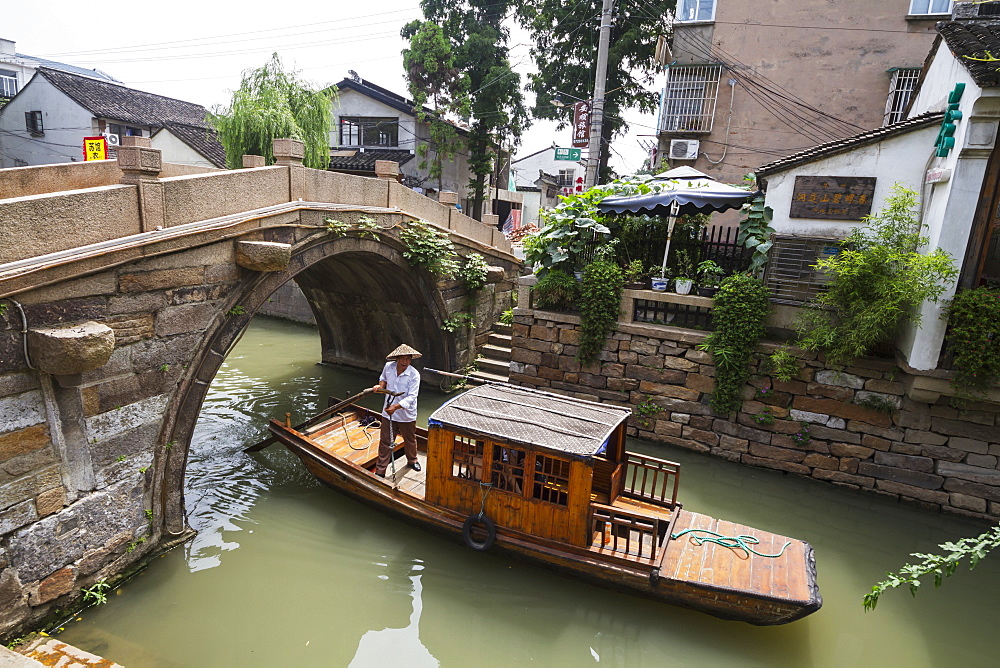 Man punting a boat by a bridge over the North-South canal by Pingjiang Road, Suzhou, Jiangsu, China