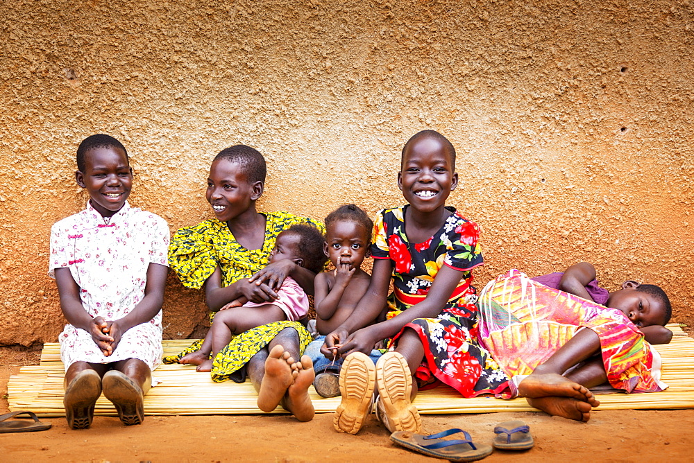 Young girls and small children sitting together on a mat against a wall, Gulu, Uganda