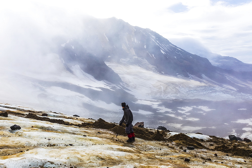 A man looks toward Trident Volcano through clouds while ascending the Knife Creek Glaciers in Katmai National Park; Alaska, United States of America