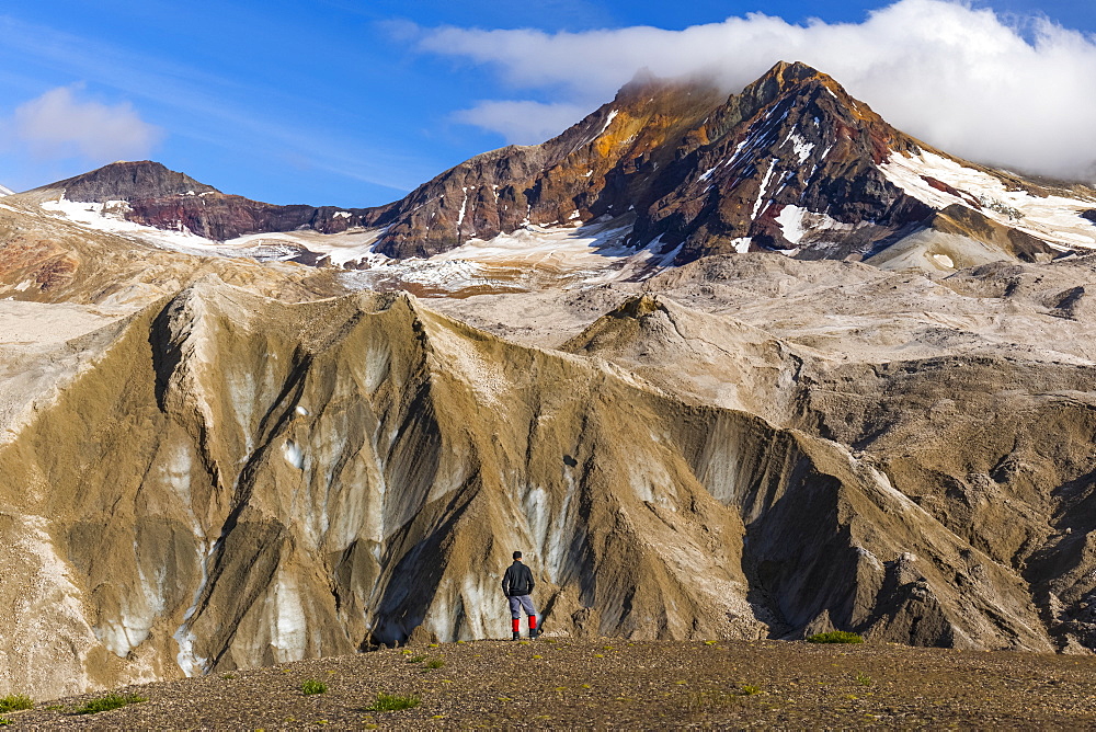 A man is dwarfed by the jagged, ash-covered Knife Creek Glaciers and Trident Volcano in the Valley of Ten Thousand Smokes in Katmai National Park; Alaska, United States of America