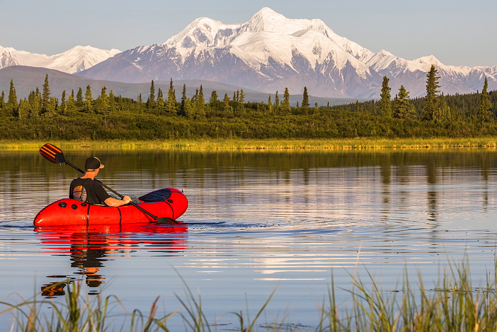 A man paddles a pack raft across Donnelly Lake with Mt. Hayes towering in the distance; Alaska, United States of America