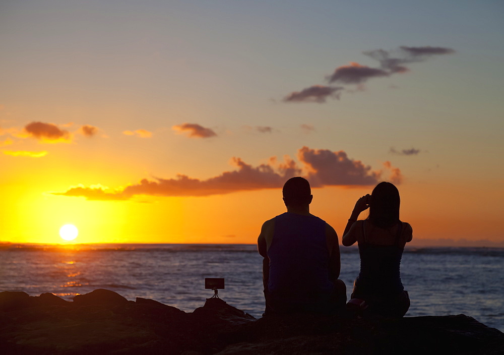 Silhouette of a couple taking pictures and watching the sunset on the beach, Waikiki; Honolulu, Oahu, Hawaii, United States of America