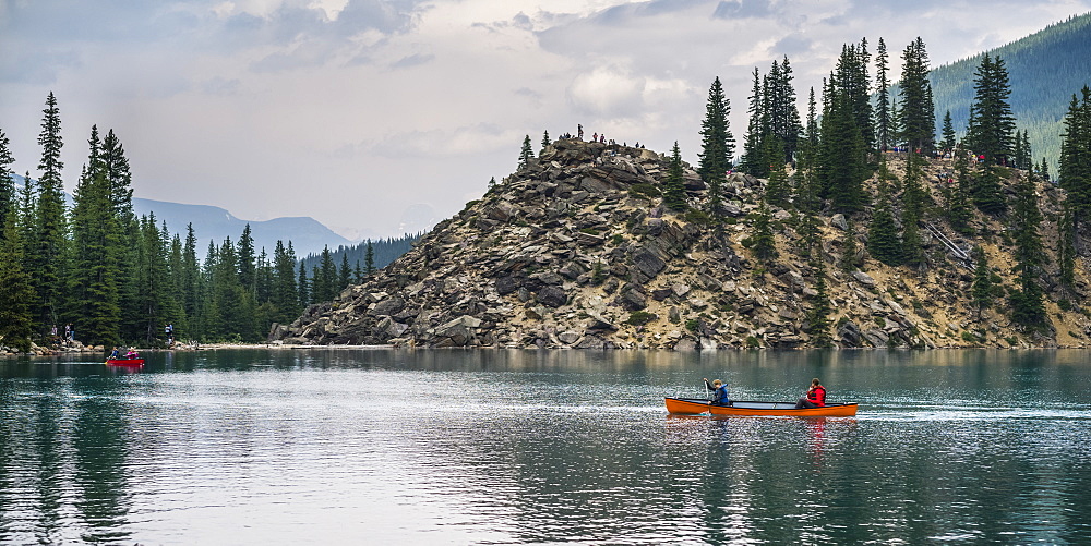 A red canoe in Moraine Lake with a cliff of the Canadian Rocky Mountains along the shoreline; Lake Louise, Alberta, Canada