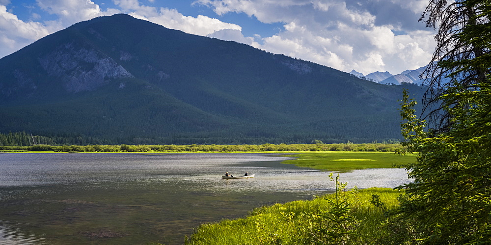 Two people sit in a canoe in the tranquil water of Vermillion Lakes in the Canadian Rocky Mountains; Field, Alberta, Canada