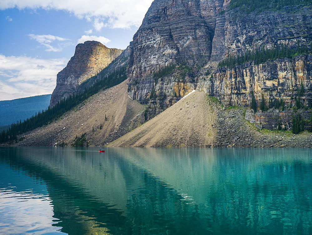 A red canoe in Moraine Lake with a cliff of the Canadian Rocky Mountains along the shoreline; Lake Louise, Alberta, Canada