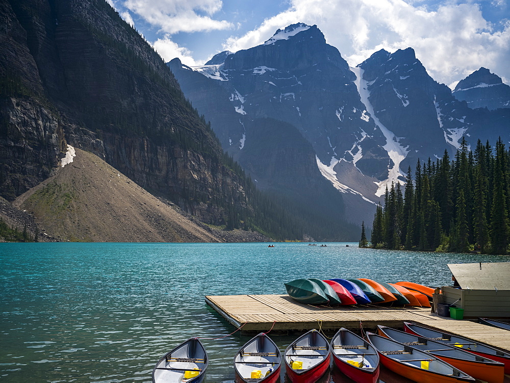 Canoes in the water and sitting on a dock along the shore of Moraine Lake in the Canadian Rocky Mountains; Eldon, Alberta, Canada