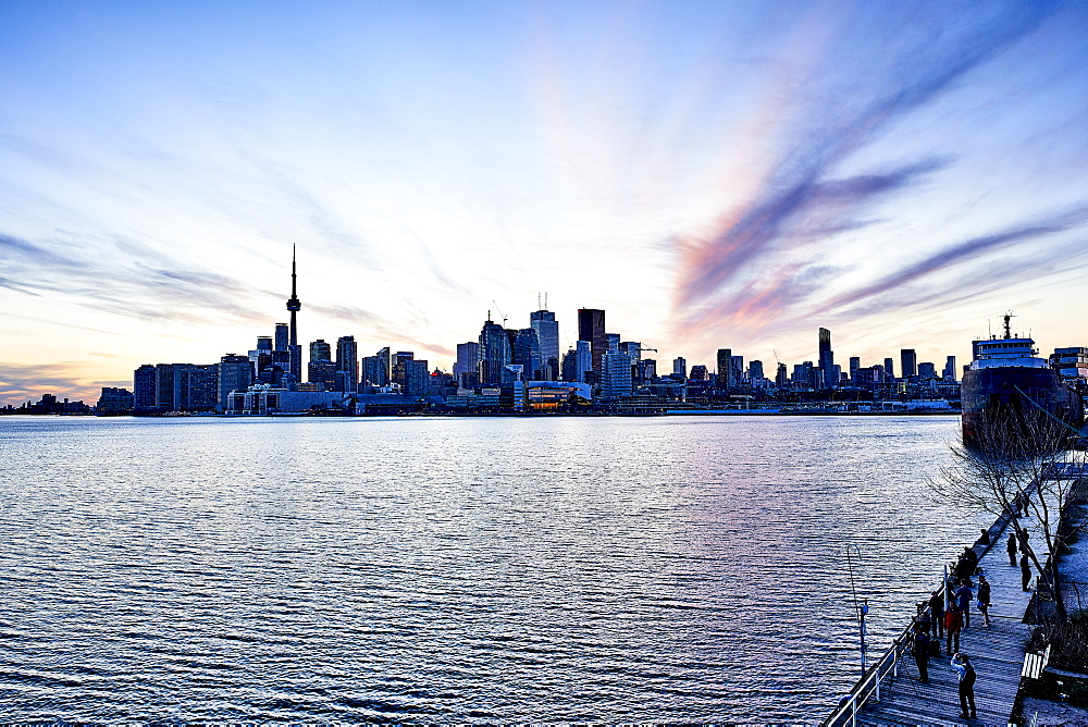 Tourists On A Boardwalk With A View Of The Downtown City Skyline At Dusk; Toronto, Ontario, Canada