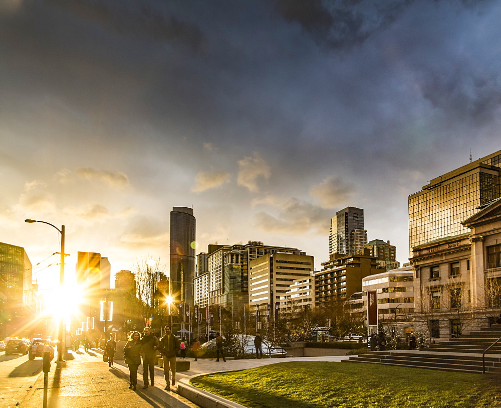 A street scene in Vancouver at sunset with pedestrians and buildings reflecting sunlight, Vancouver, British Columbia, Canada