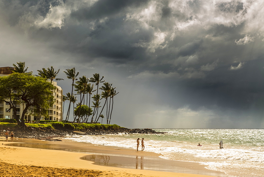 Tourists on a beach on the island of Maui with dark clouds and rainfall over the ocean in the distance, Makawao, Maui, Hawaii, United States of America