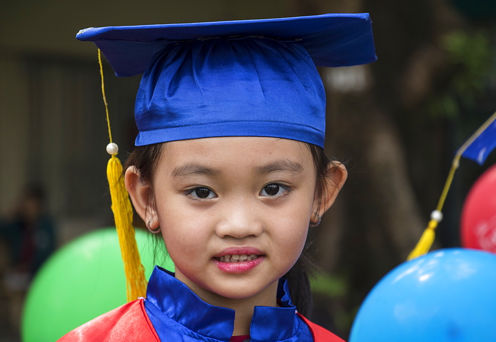 Portrait of a Vietnamese school girl in a cap and gown for graduation, Ho Chi Minh City, Vietnam