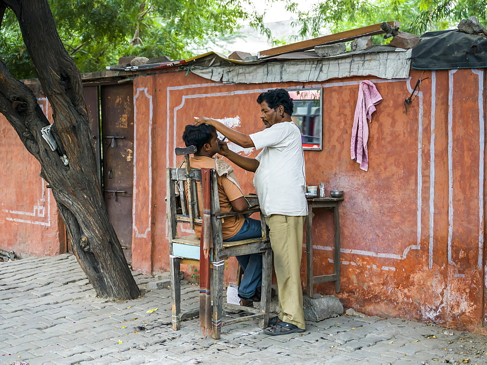 A man shaving another man's face with a set up of table and chair along the street, Jaipur, Rajasthan, India