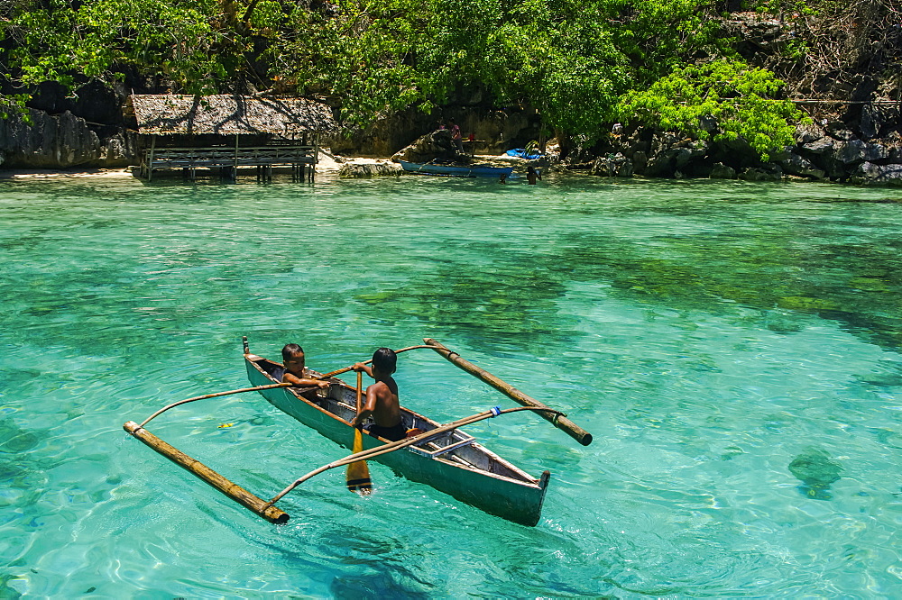 Boys paddling in an outrigger canoe, fishing in the turquoise waters of the Indian Ocean, Andaman Islands, India