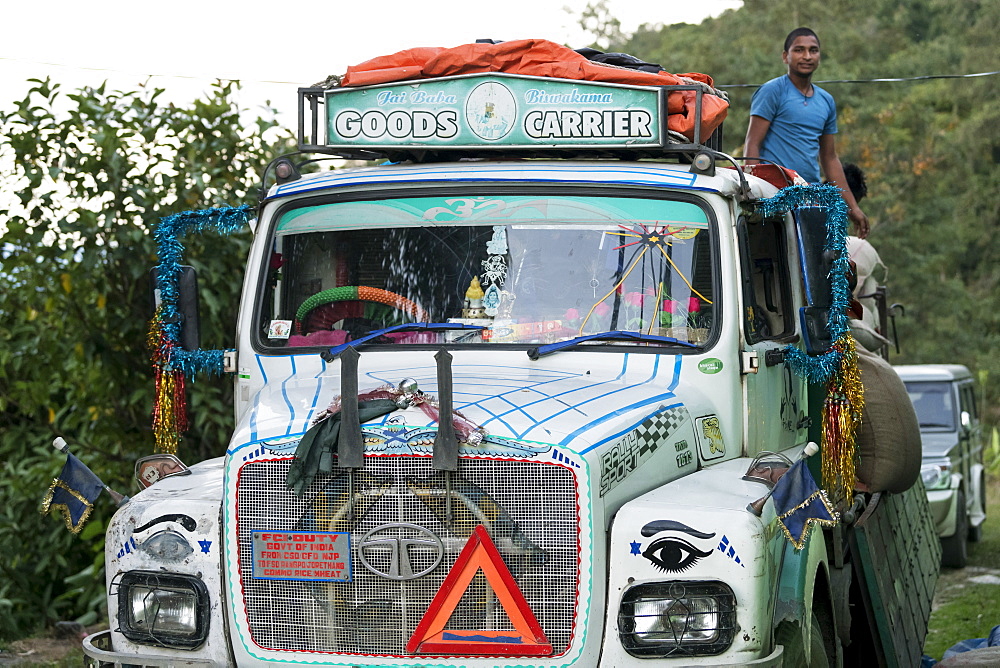 A colourful and decorated transport truck on a road with a worker standing up in the back, Sikkim, India