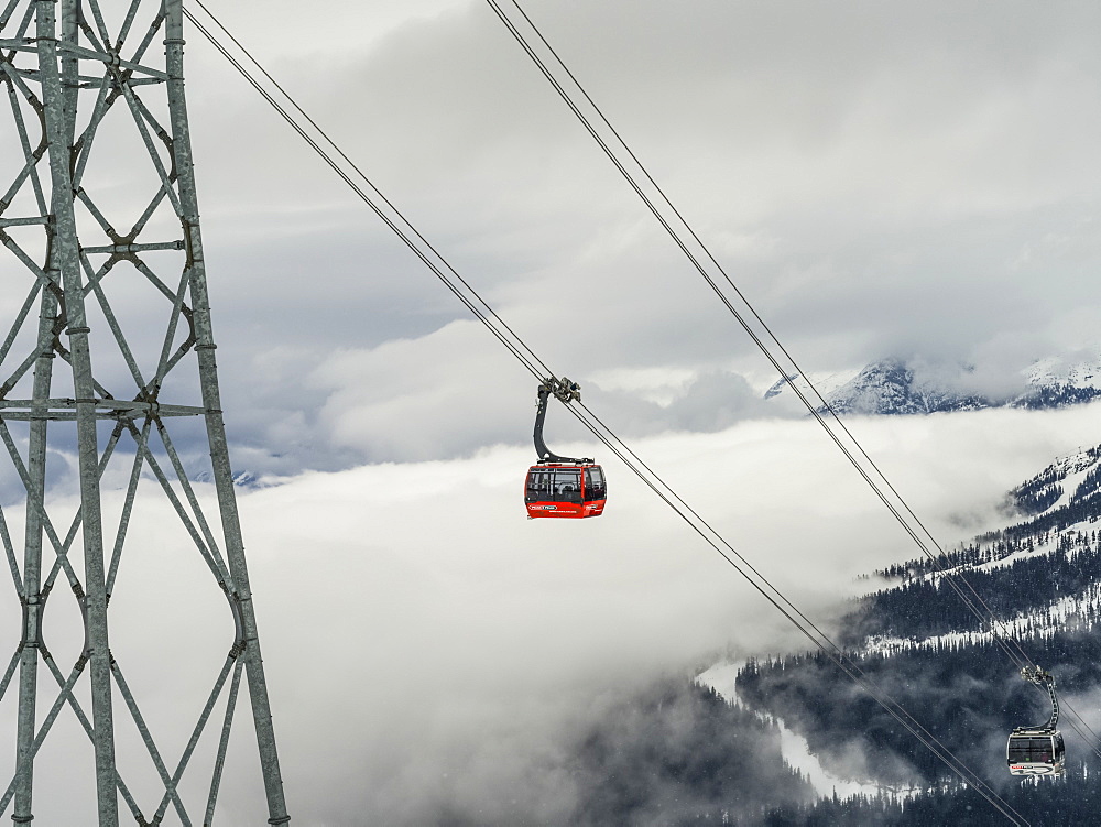 Red gondola lift on the cables above the mountains and clouds, Whistler, British Columbia, Canada