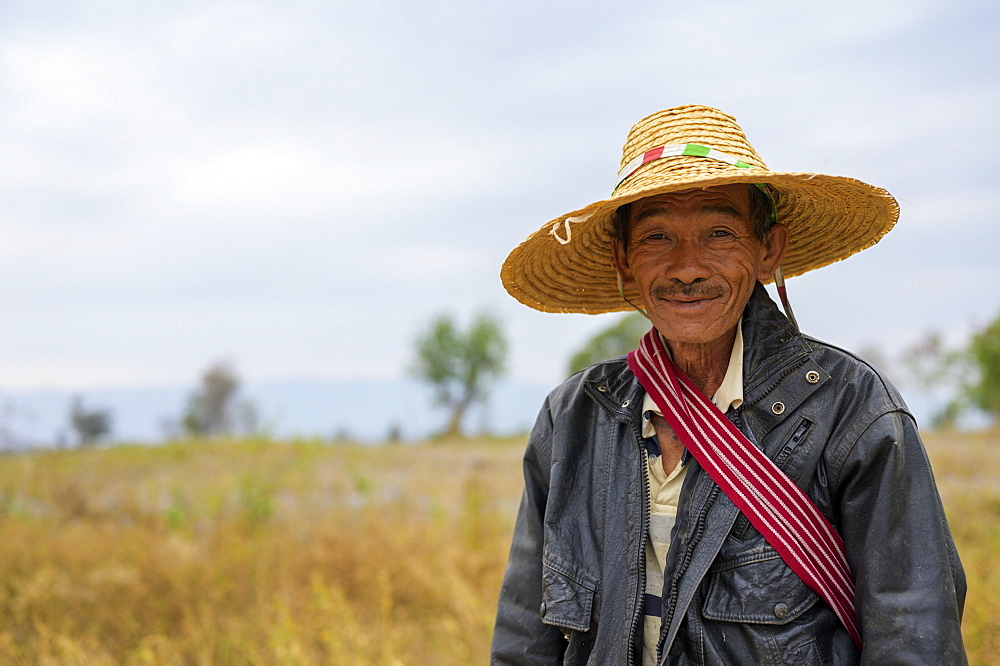 A farmer standing in a field wearing a straw hat, Taungyii, Shan State, Myanmar