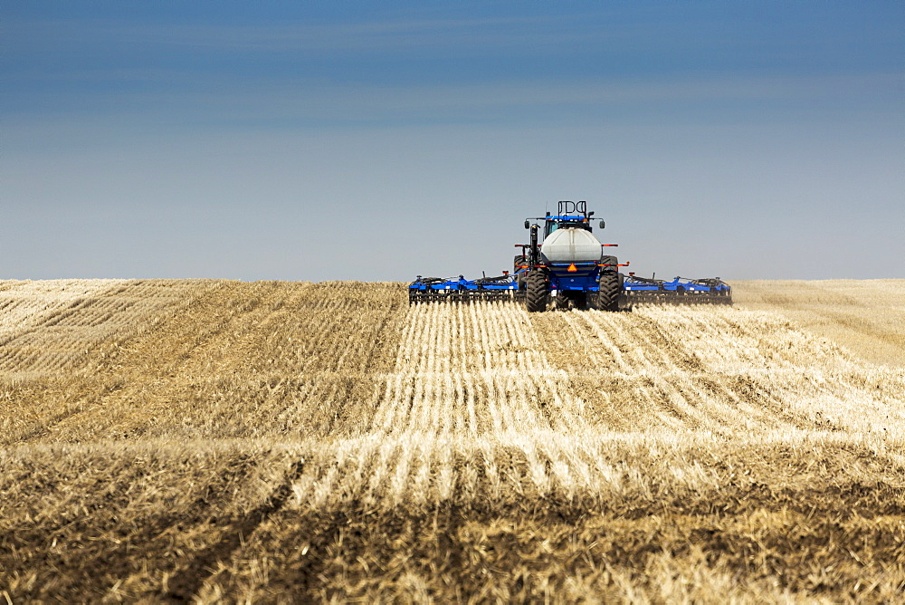 Back view of air seeder, seeding a stubble field with blue sky and hazy clouds, near Beiseker, Alberta, Canada