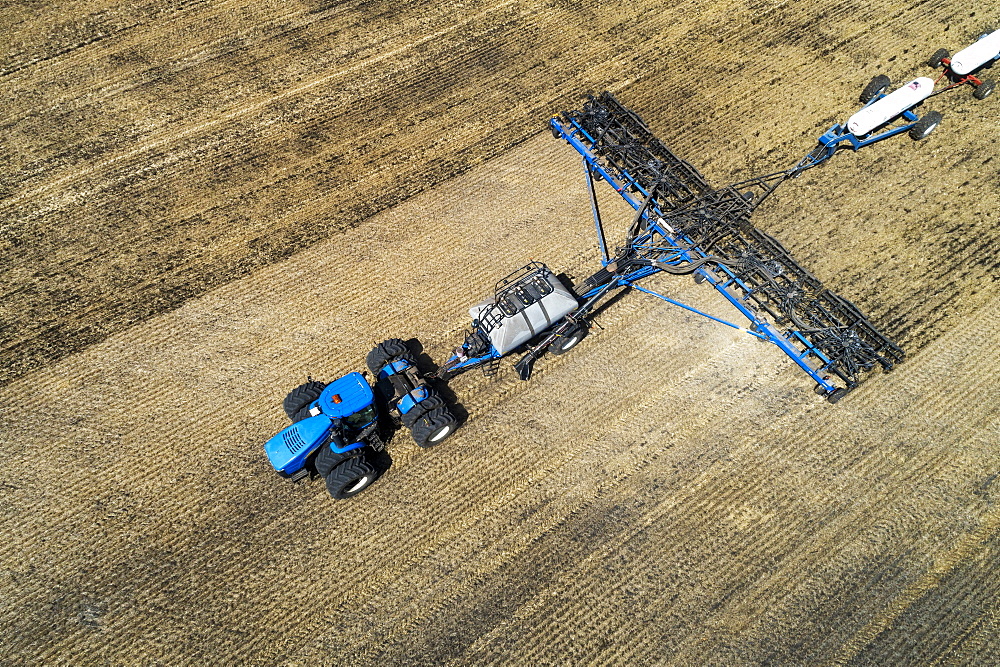 Aerial view of air seeder in field with white ammonia tanks, near Beiseker, Alberta, Canada