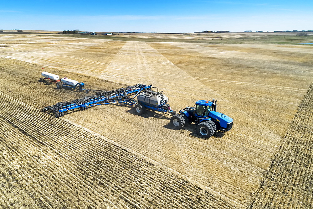 Air seeder in field with white ammonia tanks, near Beiseker, Alberta, Canada