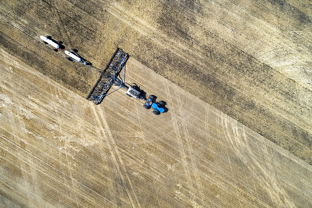 Aerial view of air seeder in field with white ammonia tanks, near Beiseker, Alberta, Canada