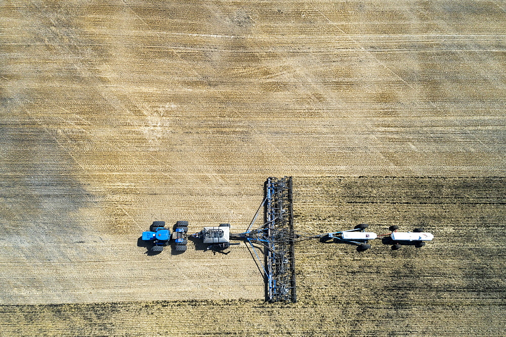 Aerial view of air seeder in field with white ammonia tanks, near Beiseker, Alberta, Canada