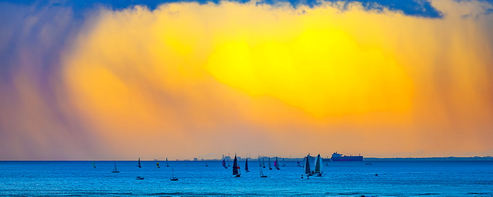 Clouds glowing a bright yellow at sunset off Waikiki Beach with a silhouetted sailboats in the water, Honolulu, Oahu, Hawaii, United States of America