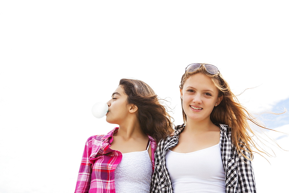 Two friends standing together with windblown hair, one blowing a bubble with bubblegum, Toronto, Ontario, Canada