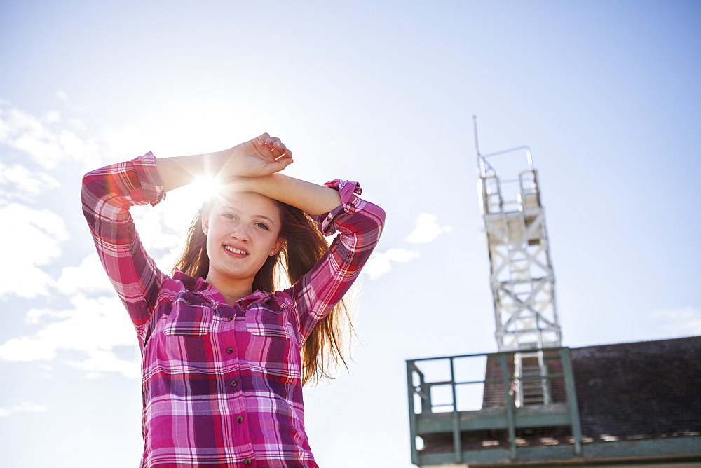 Teenage girl standing at Woodbine Beach with lifeguard tower in the background and a sun flare above her head, Toronto, Ontario, Canada