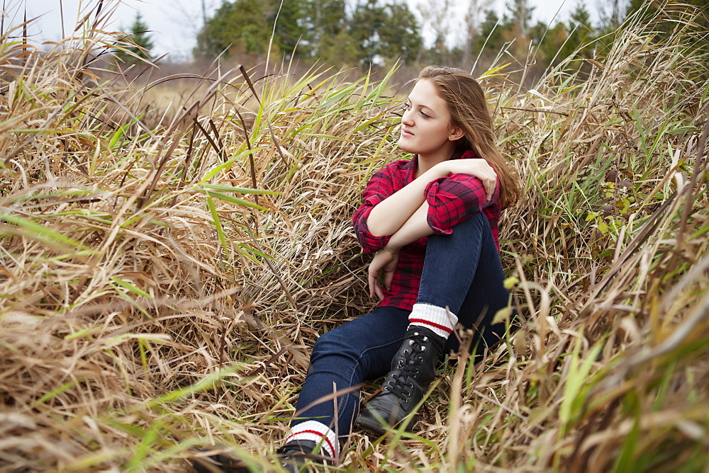 Portrait of a girl sitting in a field of tall grass looking away from the camera, Toronto, Ontario, Canada