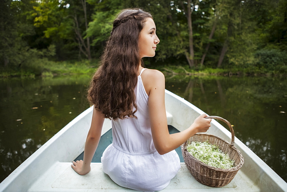 A girl sitting in a white canoe on a tranquil river with a basket full of flowers, Ontario, Canada