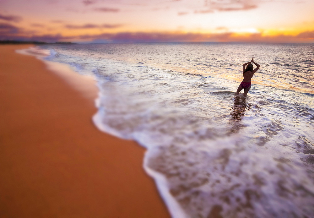 A blurred image of a woman standing in the surf, looking out at the sunset on the two mile long, three hundred feet wide, Papohaku Beach on the west shore of Molokai. This is the longest white-sand beach in the Hawaiian Islands, Molokai, Hawaii, United States of America