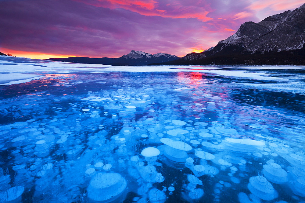 Bubbles and Cracks in the Ice with Kista Peak in the Background at Sunrise, Abraham Lake, Alberta, Canada, North America