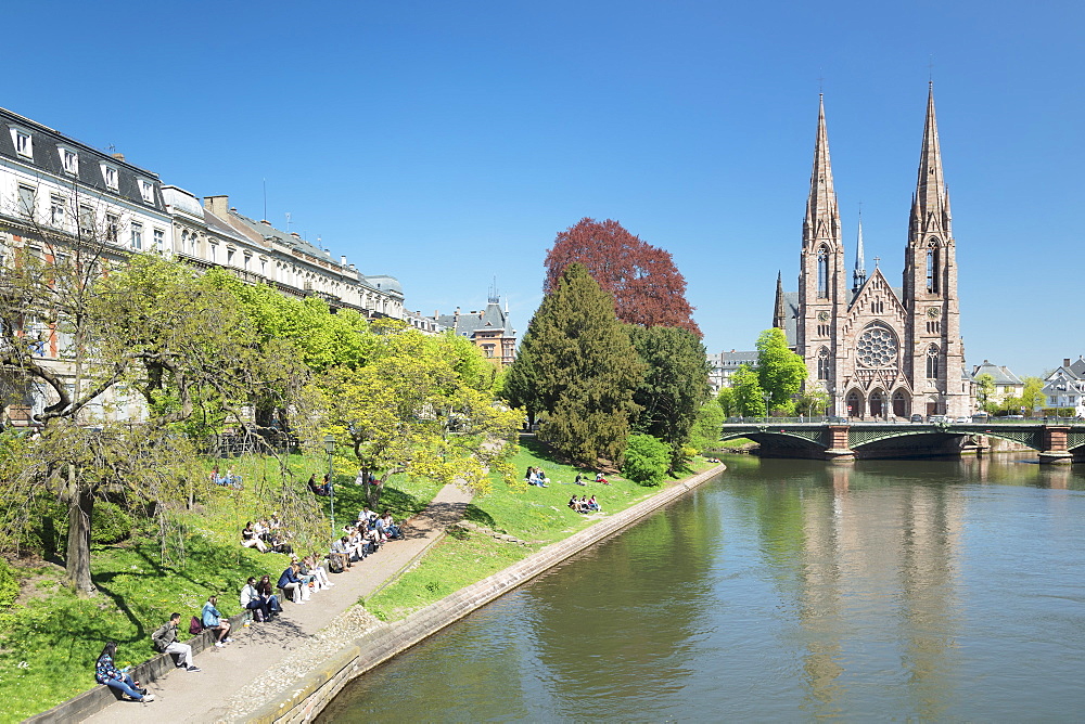 People relaxing by the Ill River, and St. Paul's Church, Strasbourg, Alsace, France, Europe