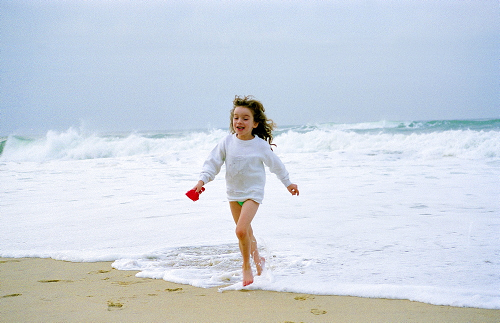 An eight year old girl running out of the sea during a holiday in France