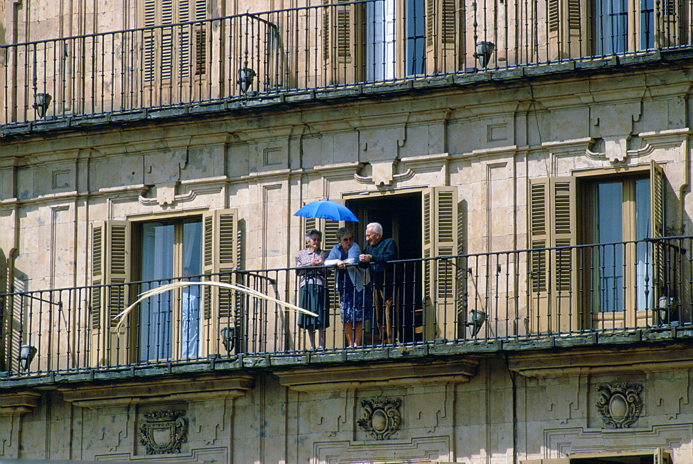 A group of elderly people standing on their balcony shielding themselves from the sun with a parasol, Salamanca, Spain