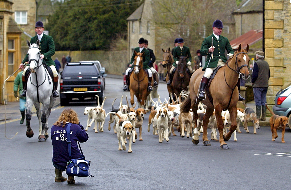 Huntsmen arriving at the Market Place, Stow-on-the-Wold,  for  a  meet for  the Heythrop New Year's Day Hunt, Oxfordshire. Woman crouches to take a picture and shows support by wearing a sweatshirt which reads 'Bollocks to Blair'