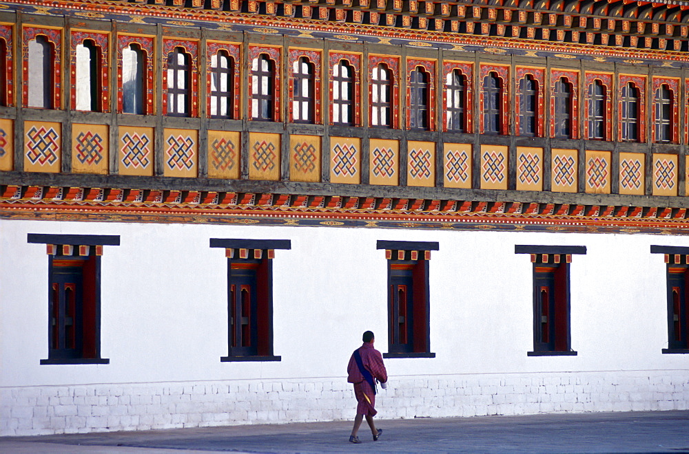 A man walking next to the Tashichho Dzong, home of the Government, Royal Palace and Religious Centre, in Thimpu, Bhutan