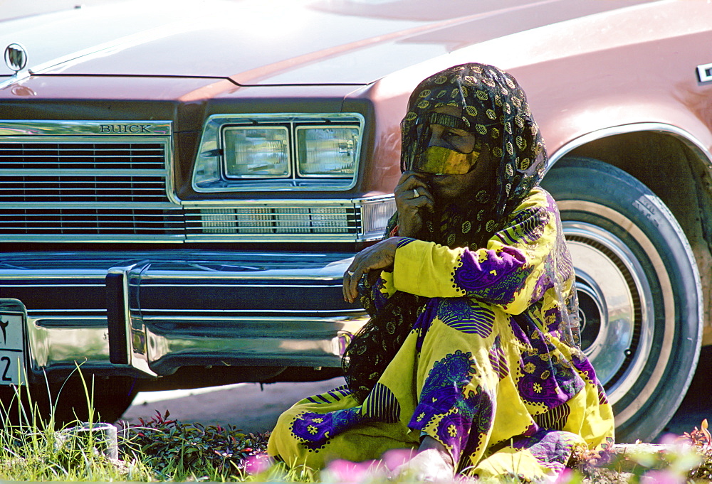 A Bedouin woman wearing traditional headgear and asaba headcovering, sits by a Buick car , Abu Dhabi