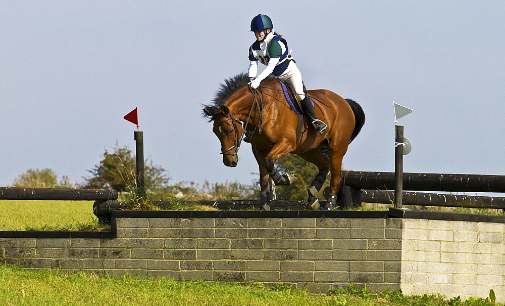 Young woman rides a bay horse in an eventing competition, Gloucestershire, United Kingdom