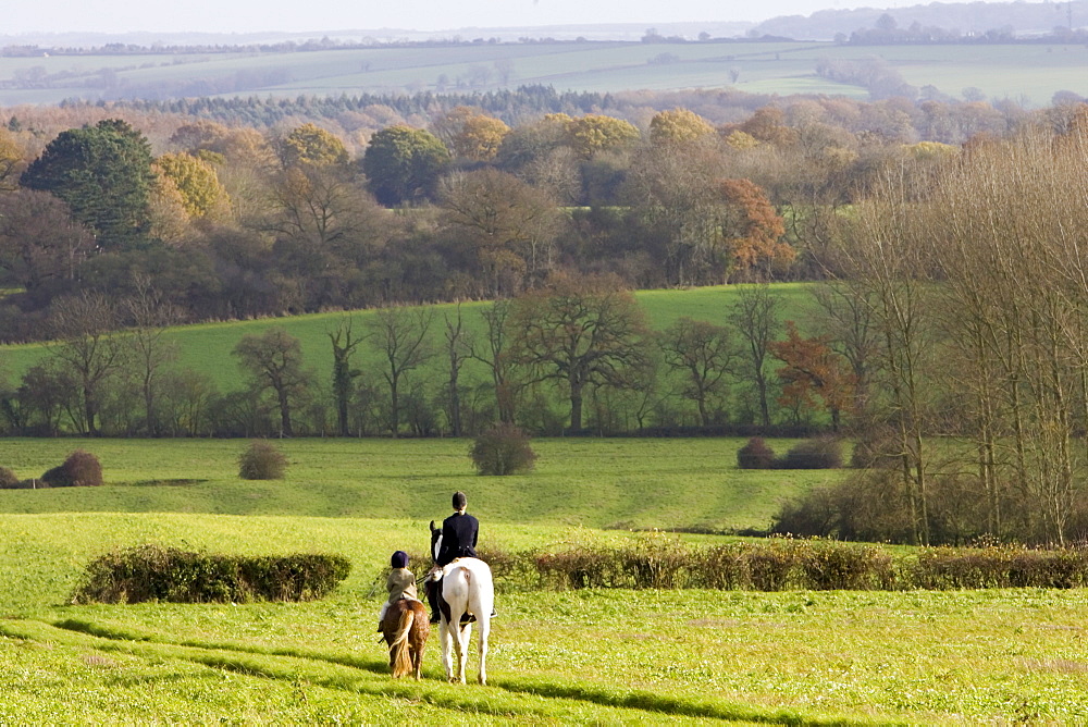 Mother and daughter ride together through rolling hills and fields in Oxfordshire, The Cotswolds, UK