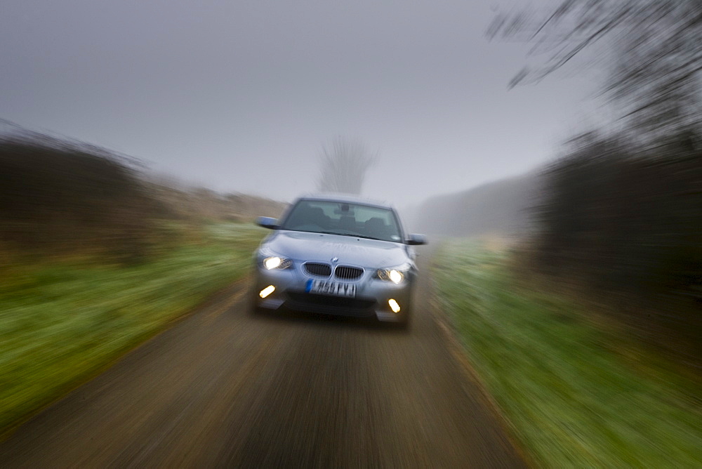 BMW 5-series car drives along empty country road in adverse foggy weather, Oxfordshire,  England, United Kingdom