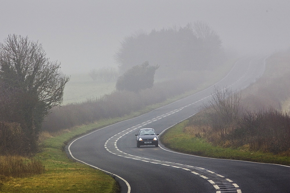 Car drives along foggy road, Oxfordshire,  United Kingdom