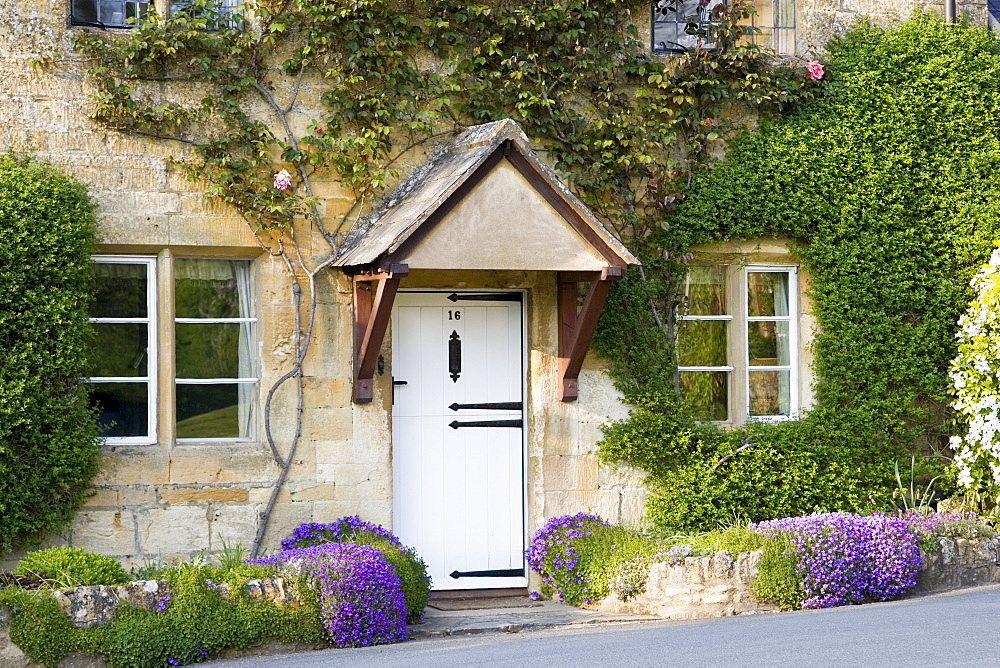 Typical cottage doorway and porch with aubretia shrubs in Stanton village, The Cotswolds, Gloucestershire, England, United Kingdom