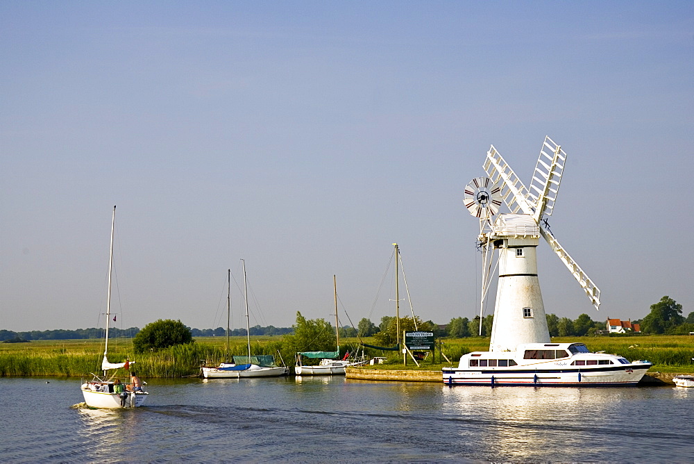 Sailing boats and river cruisers pass windmill on Norfolk Broads, United Kingdom