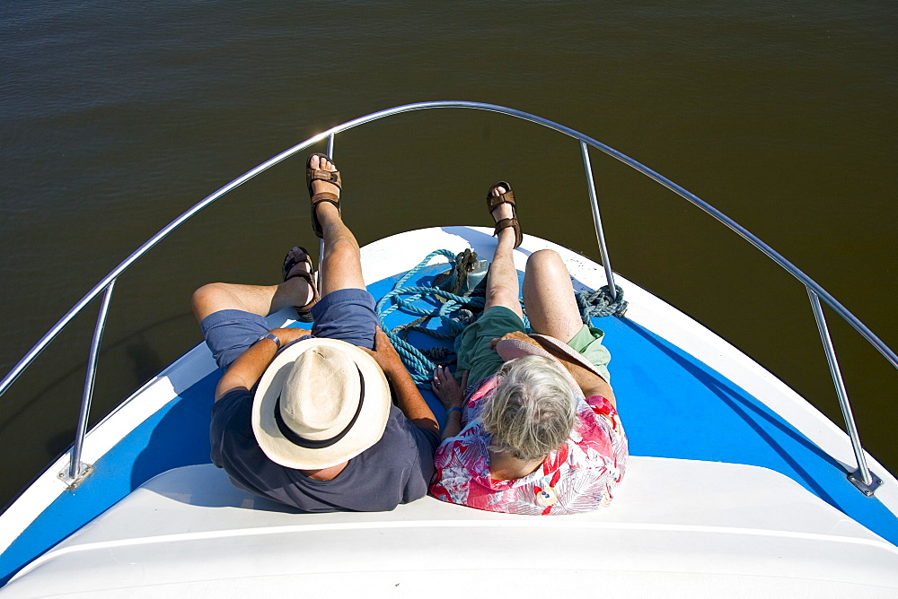 Passengers sit at the bow of a river cruiser on the Broadlands, Norfolk, United Kingdom