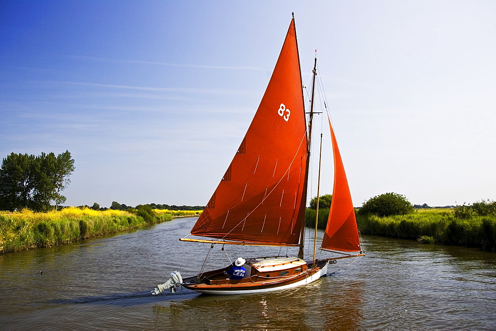 WORK LESS message on sailer's sweatshirt, sailing boat on Norfolk Broads, United Kingdom