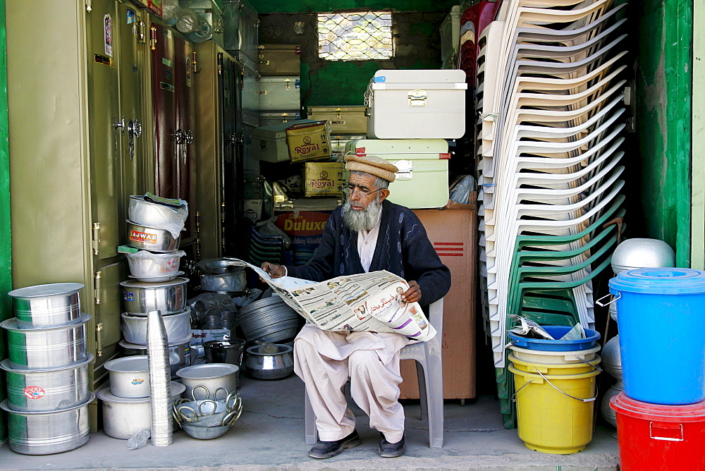 Pakistani retailer sits reading newspaper in village of Pattika, Pakistan