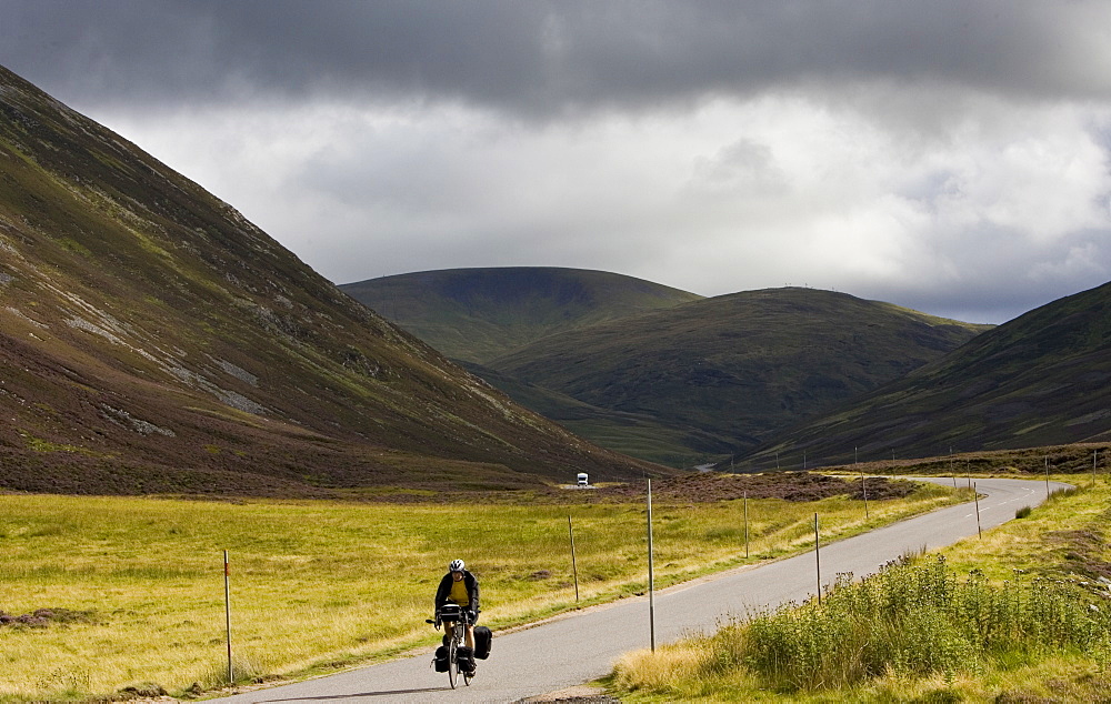 Cyclist on road through the Glen Clunie hills and Grampian Mountains, Scotland, United Kingdom